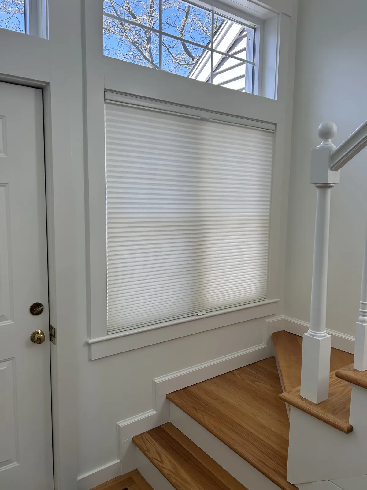 White cellular shade on a window beside a front door and staircase