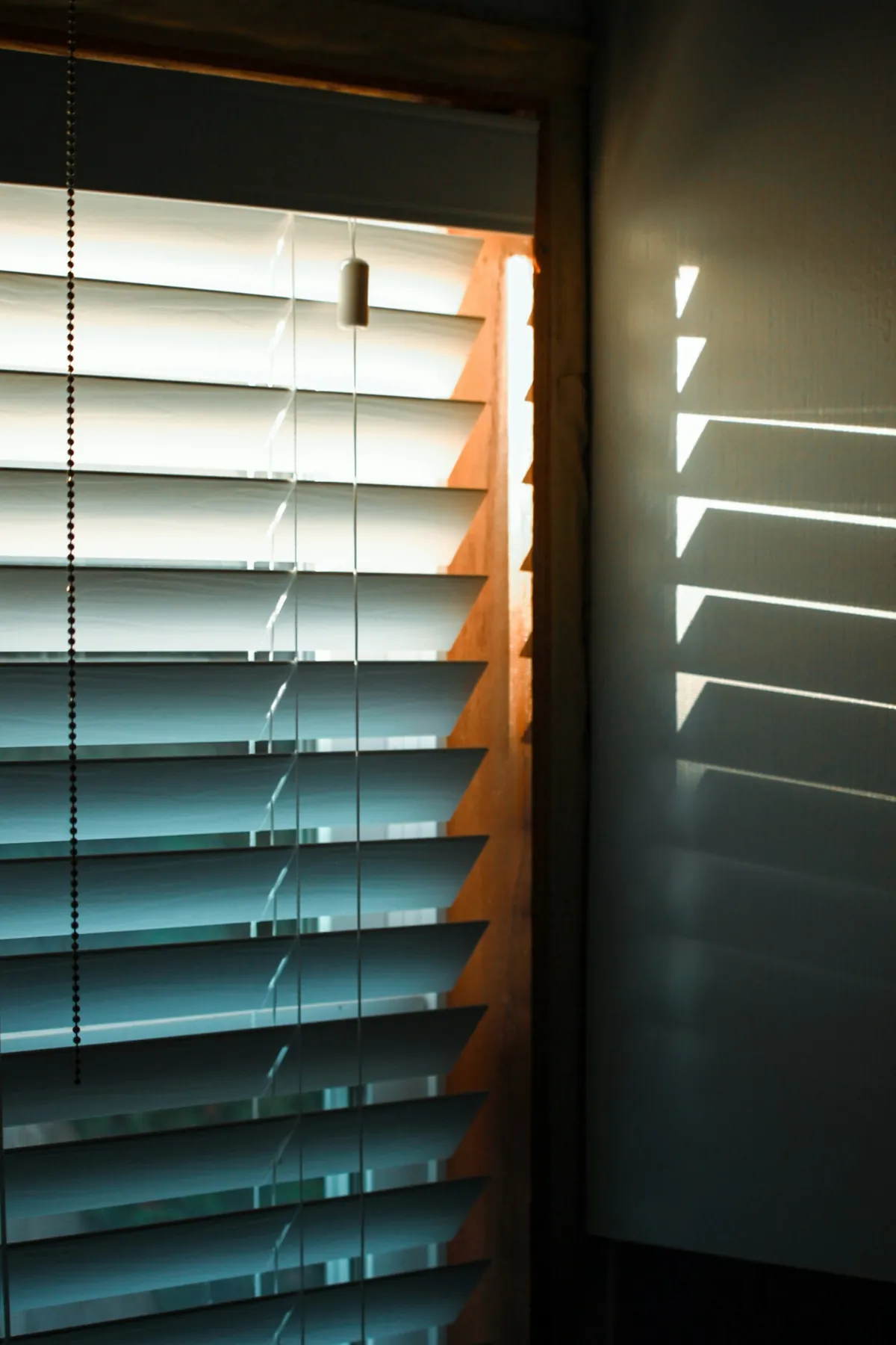 Slatted blinds half open in a dark room, light showing between the slats