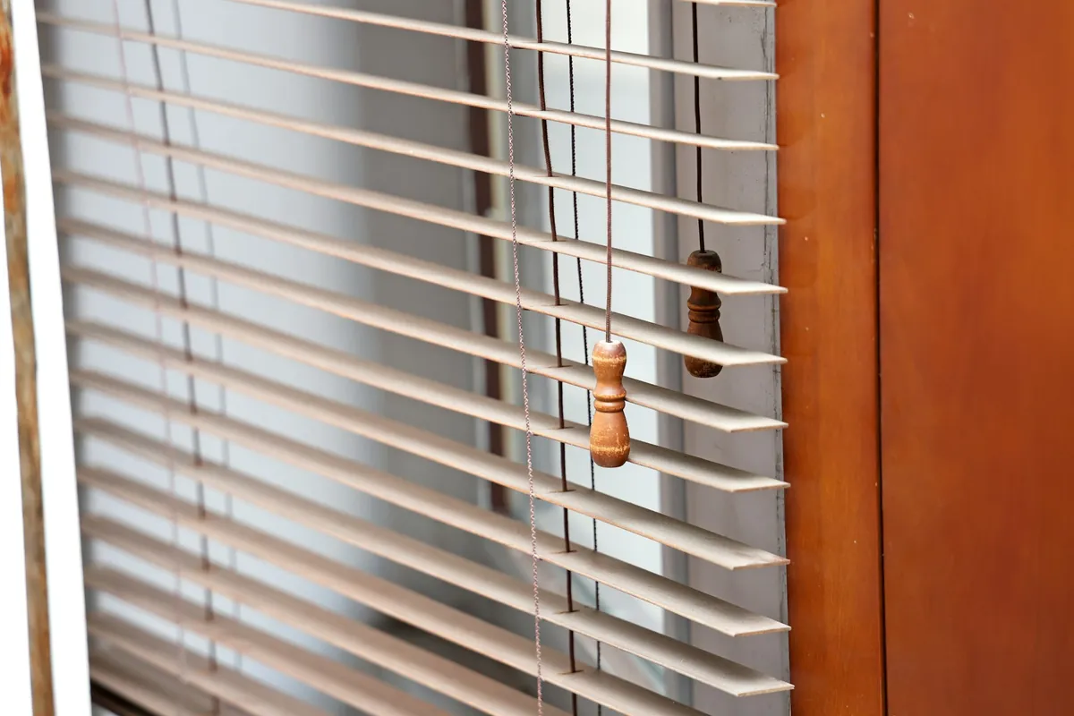 White horizontal blinds with a wooden pull on the cord