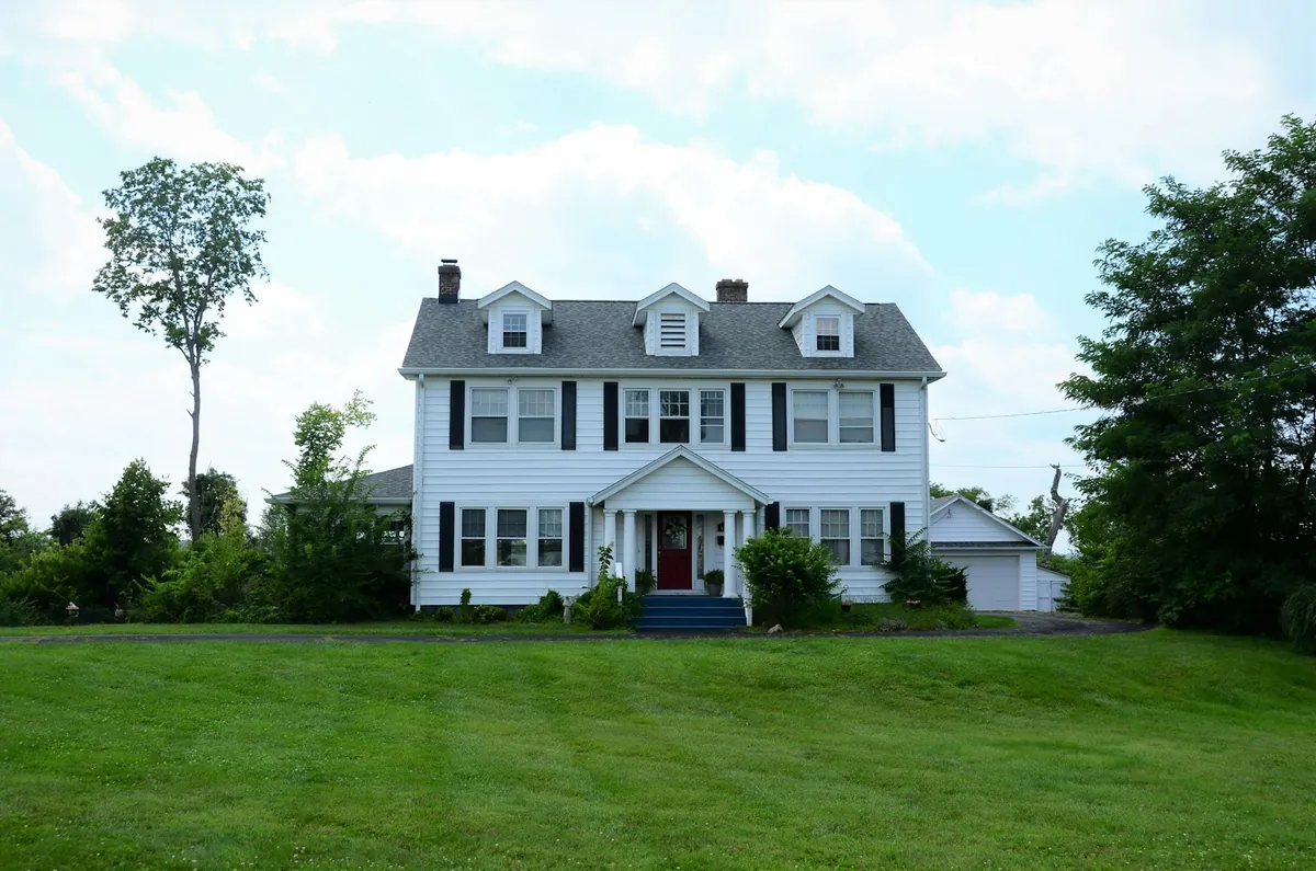 White colonial house with black shutters on a wide lawn