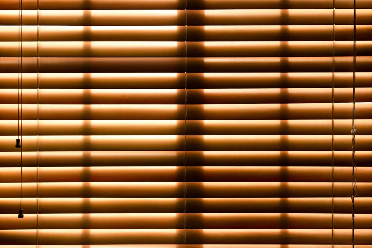 Warm brown wood blinds lowered and glowing with light from behind
