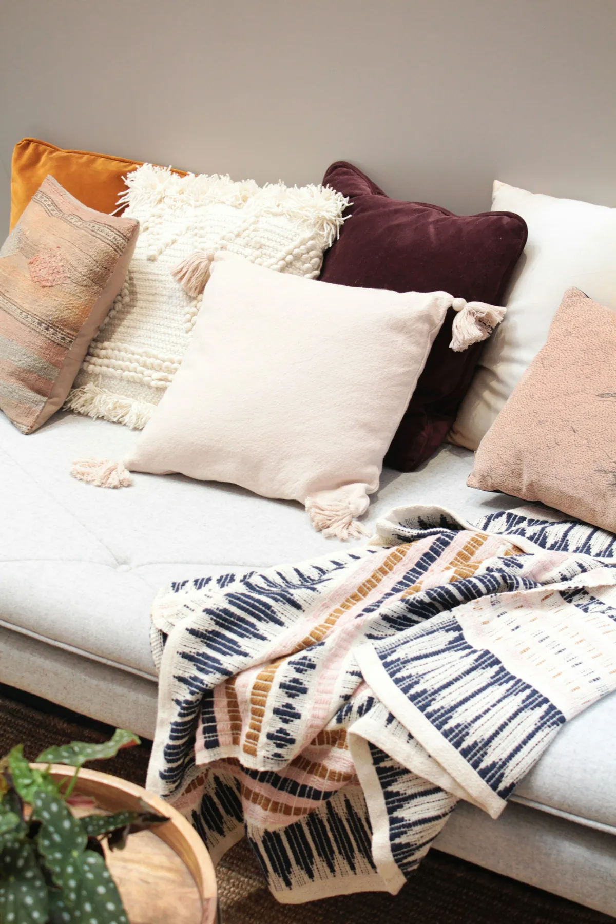 Pink, cream and burgundy pillows with a patterned throw on a white sofa