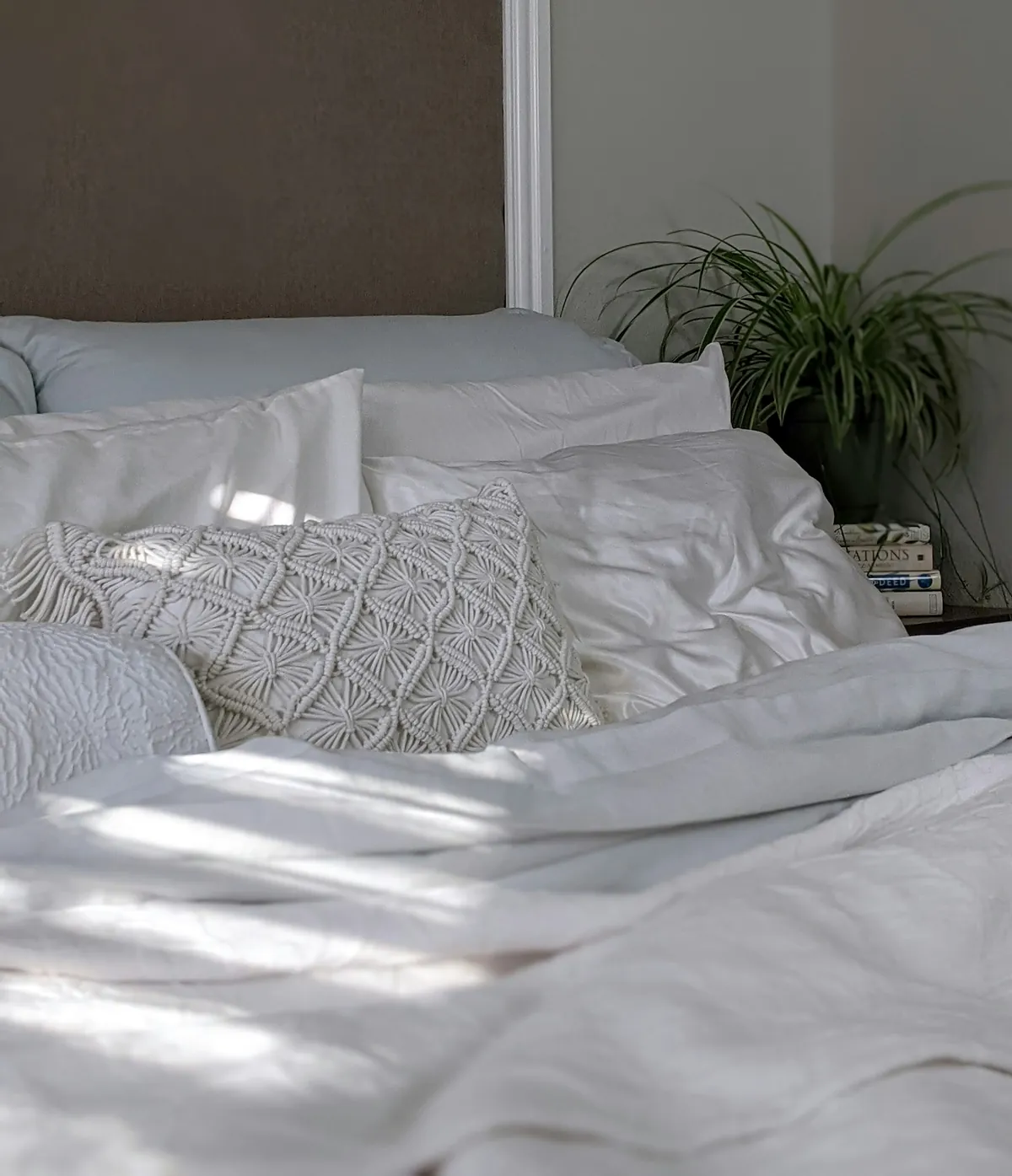 White bedding with a textured pillow and sunlight across the duvet