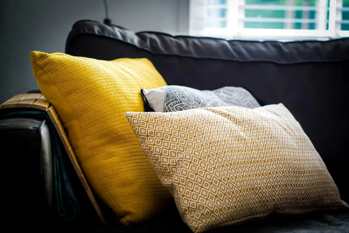 Yellow, grey and woven tan throw pillows on a dark sofa