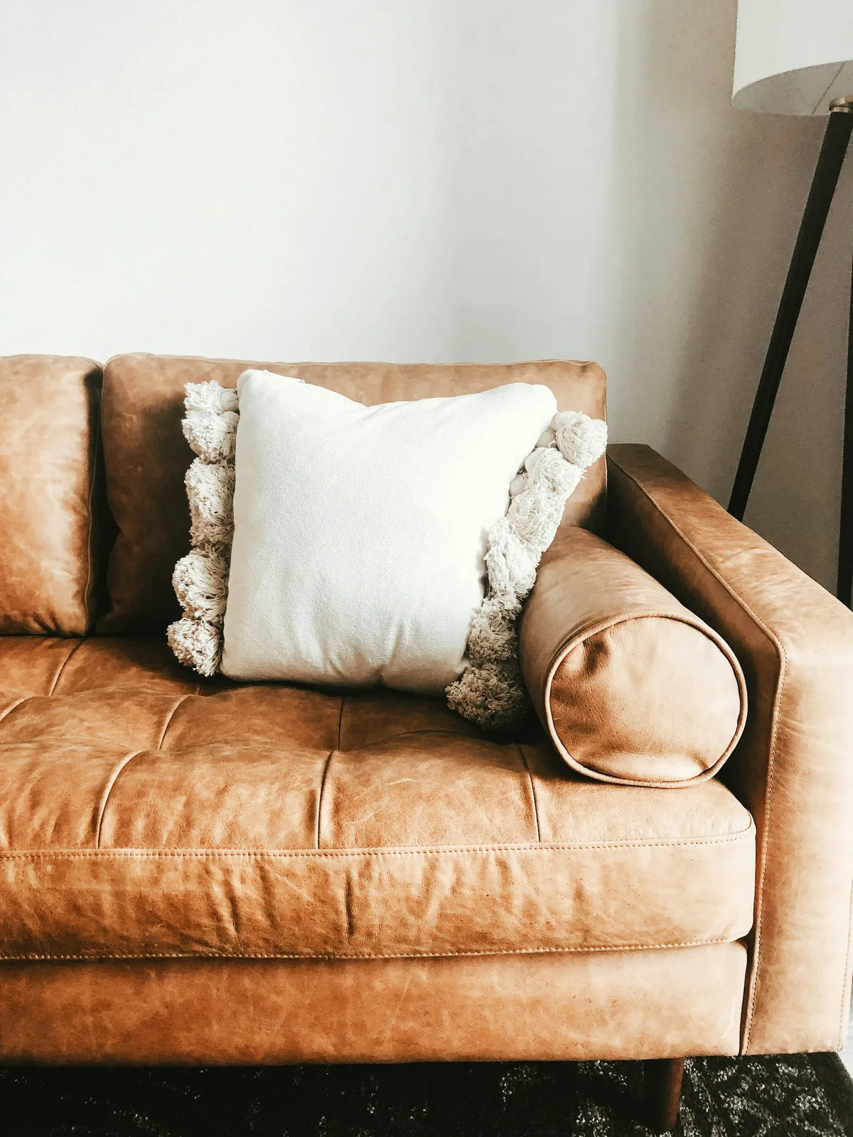 Cream tasselled pillow and a bolster on a tan leather armchair