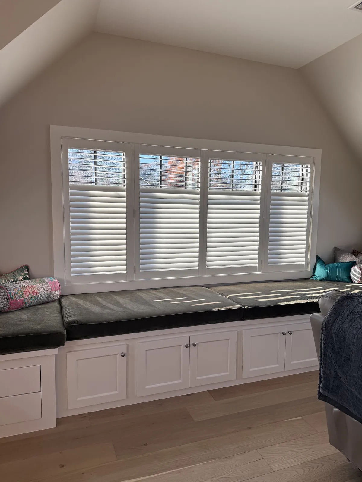 White plantation shutters on a wide window above a built-in window seat with drawers