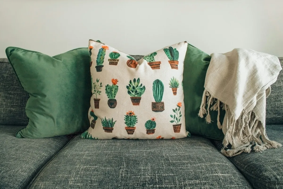 Green velvet and cactus-print pillows with a cream throw on a green sofa