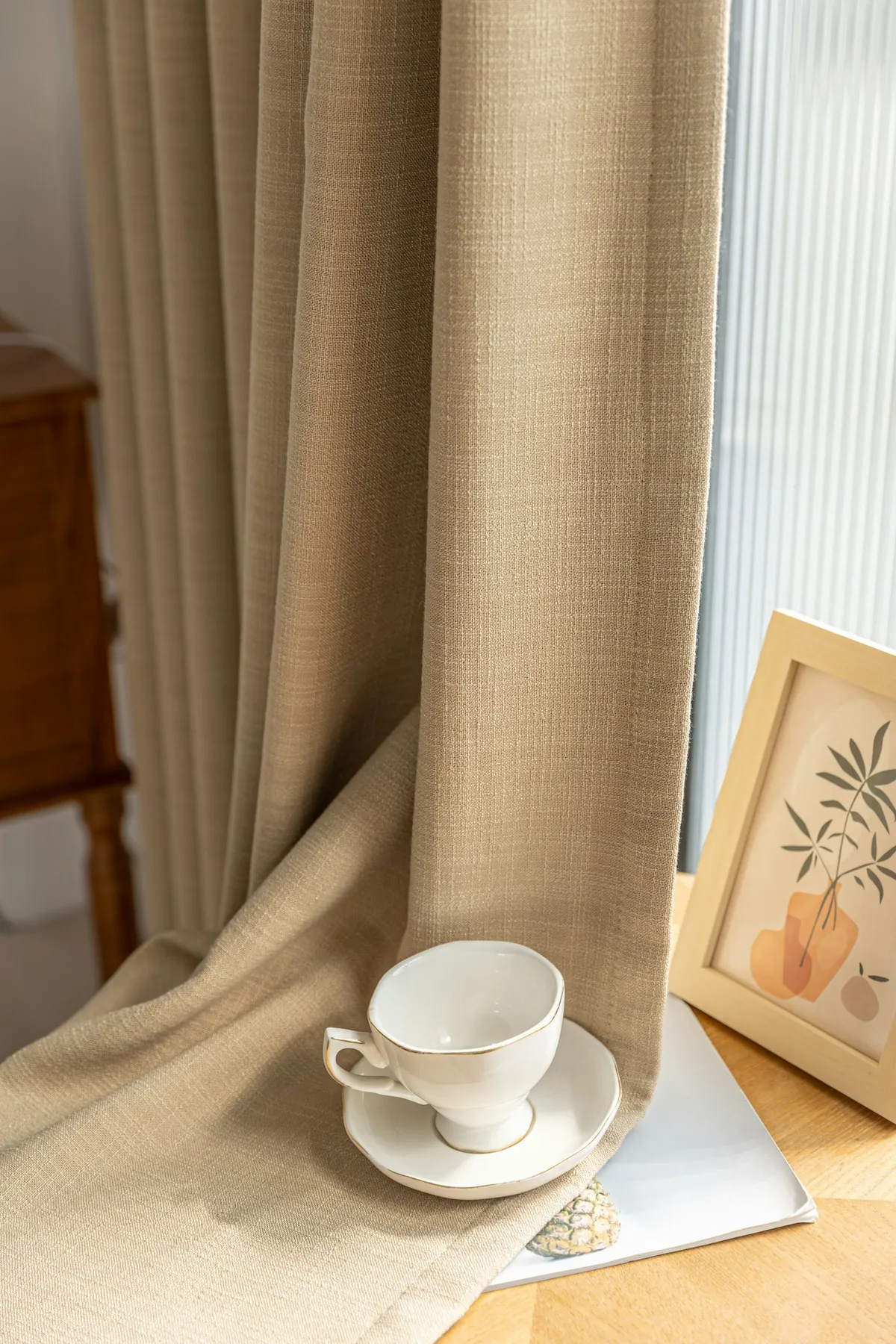 Beige linen curtain falling beside a window, a teacup on the sill