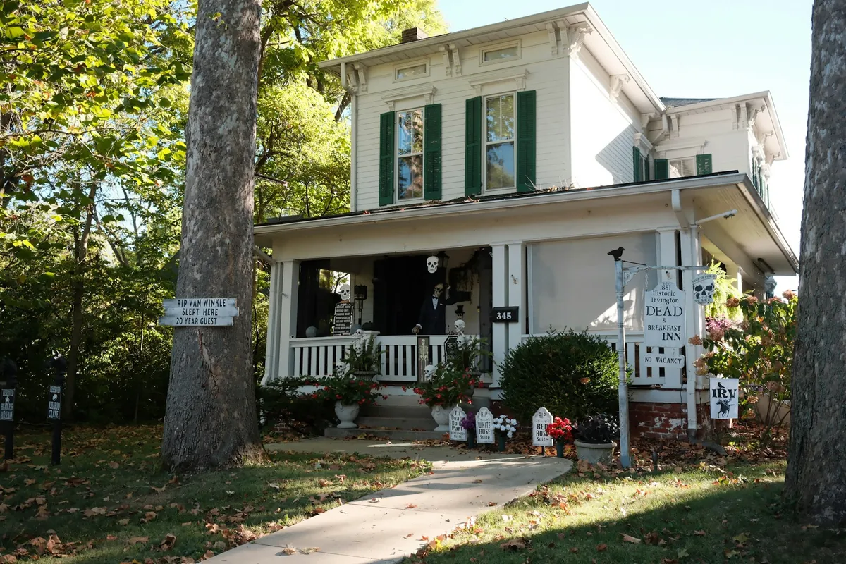 White Italianate house with green shutters and a front porch among trees