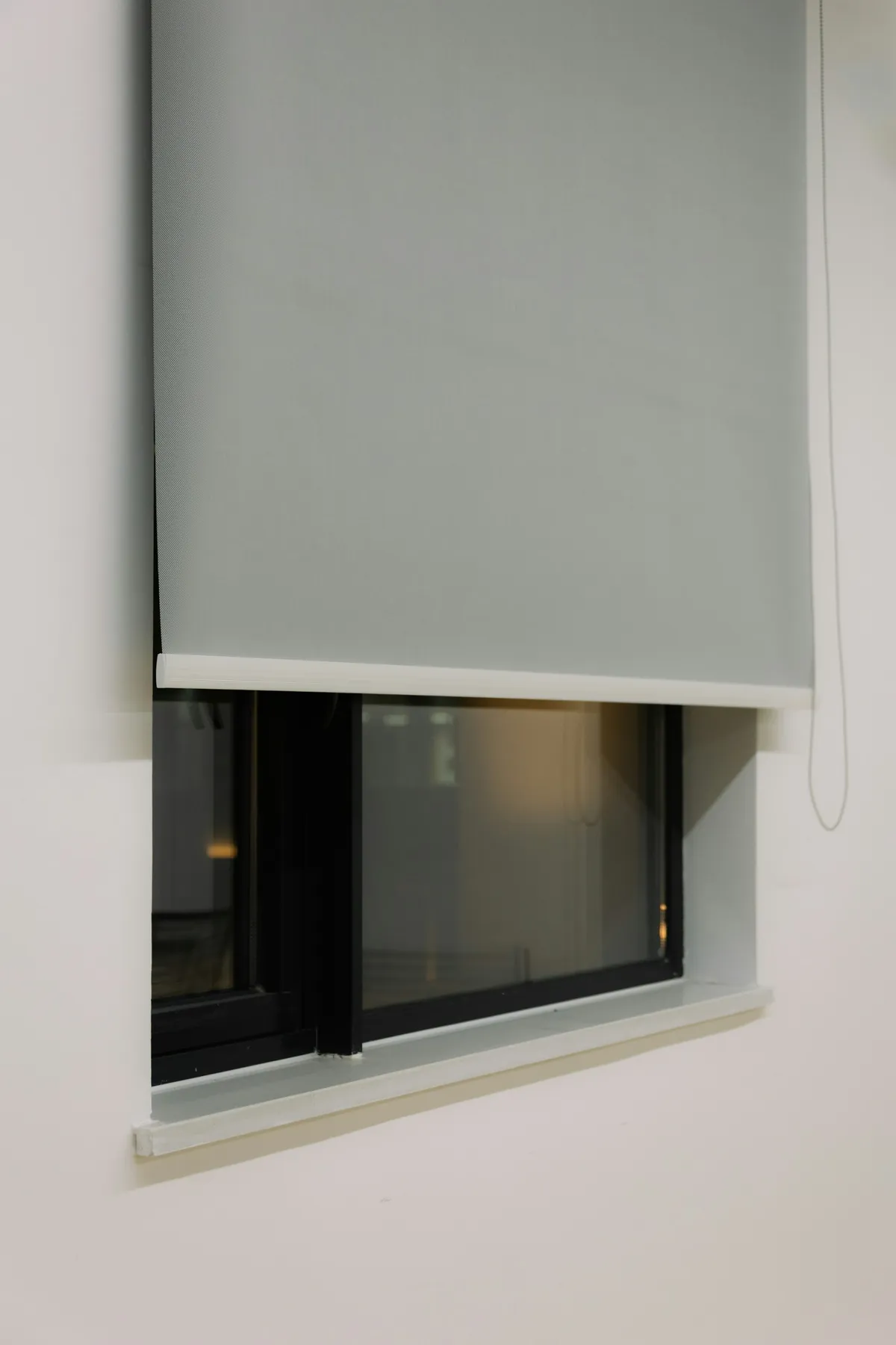 Grey roller shade partly lowered over a deep-set window