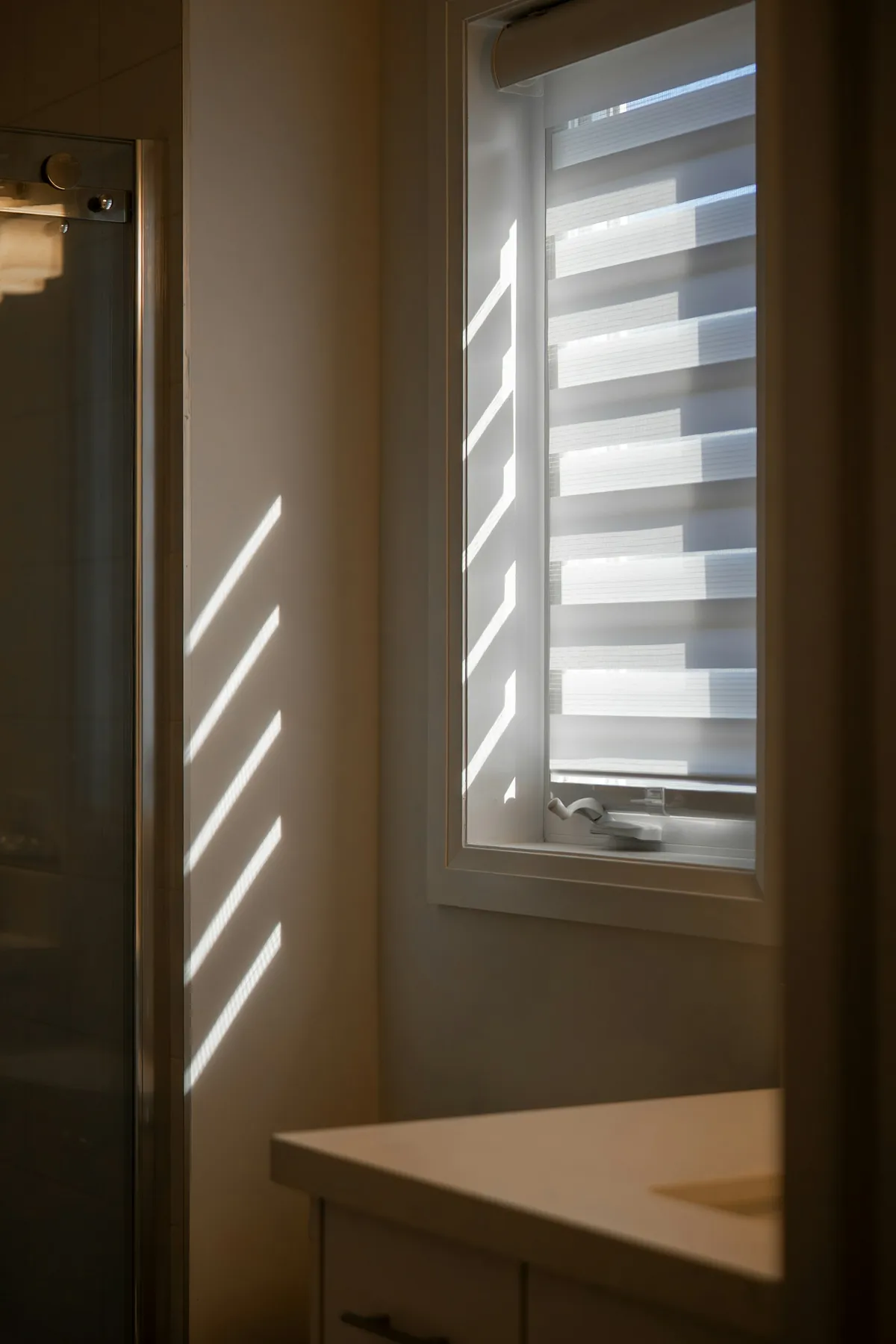 White blind on a narrow window in a dim hallway, light striping the wall