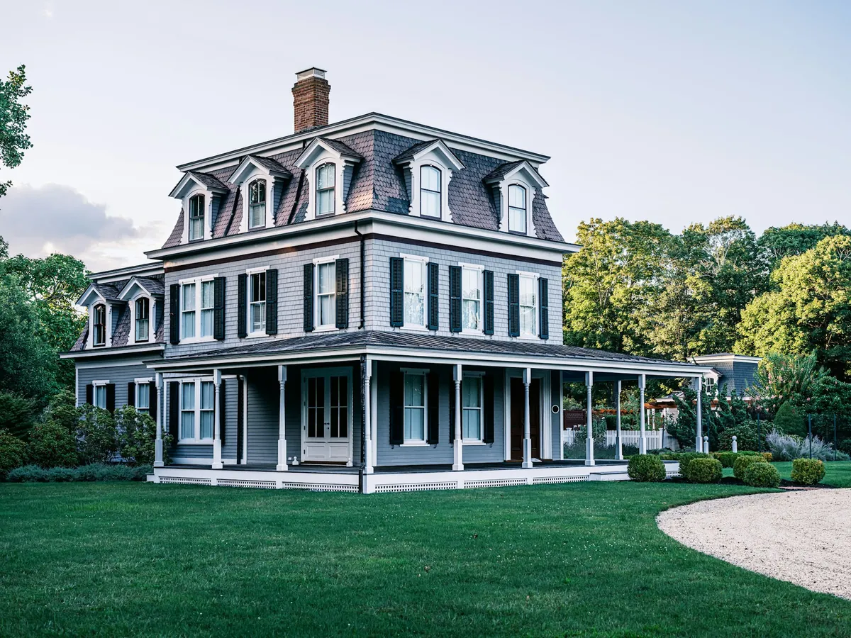 Grey Second Empire house with a mansard roof and a wraparound porch