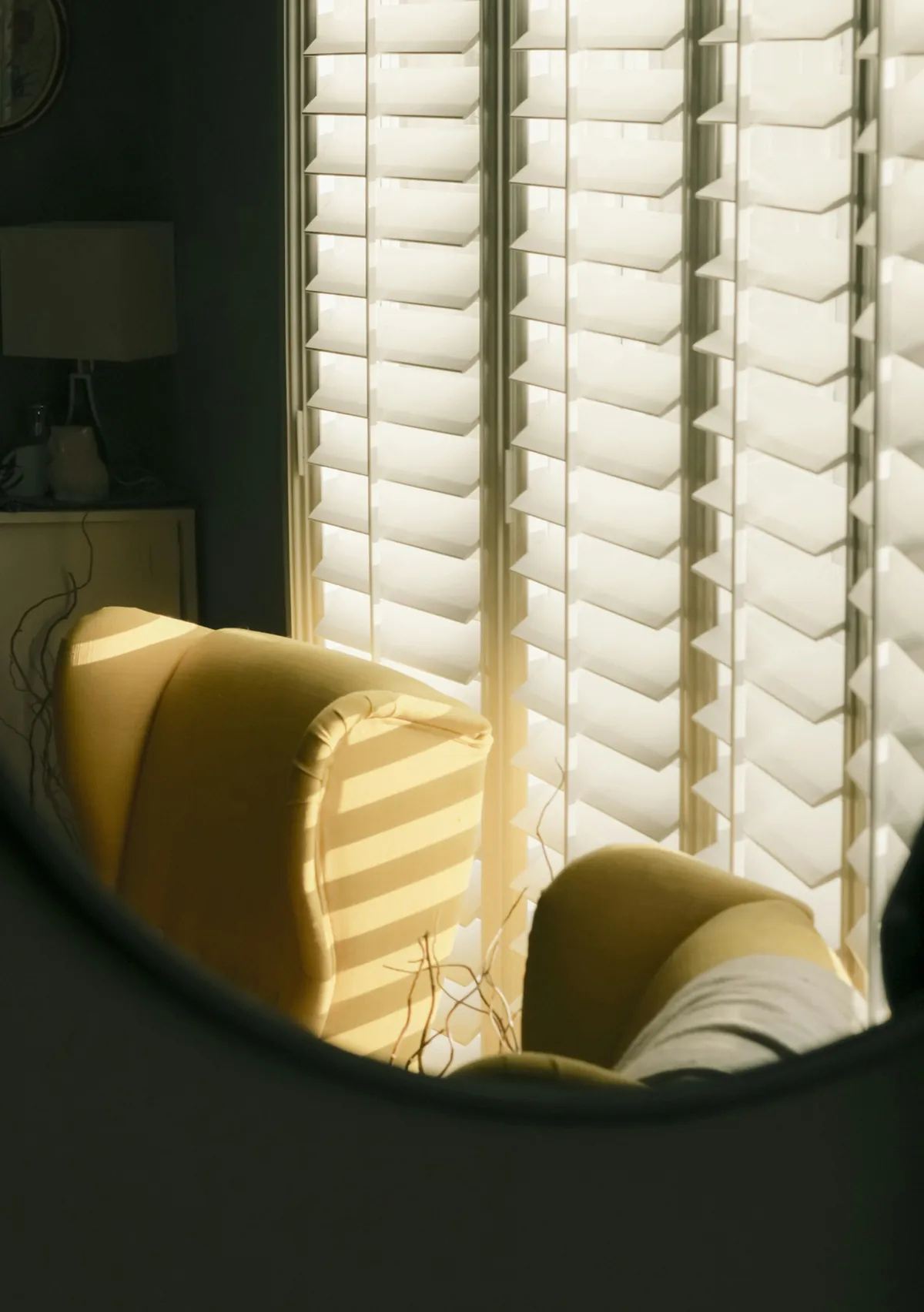 White plantation shutters with light falling on a yellow armchair