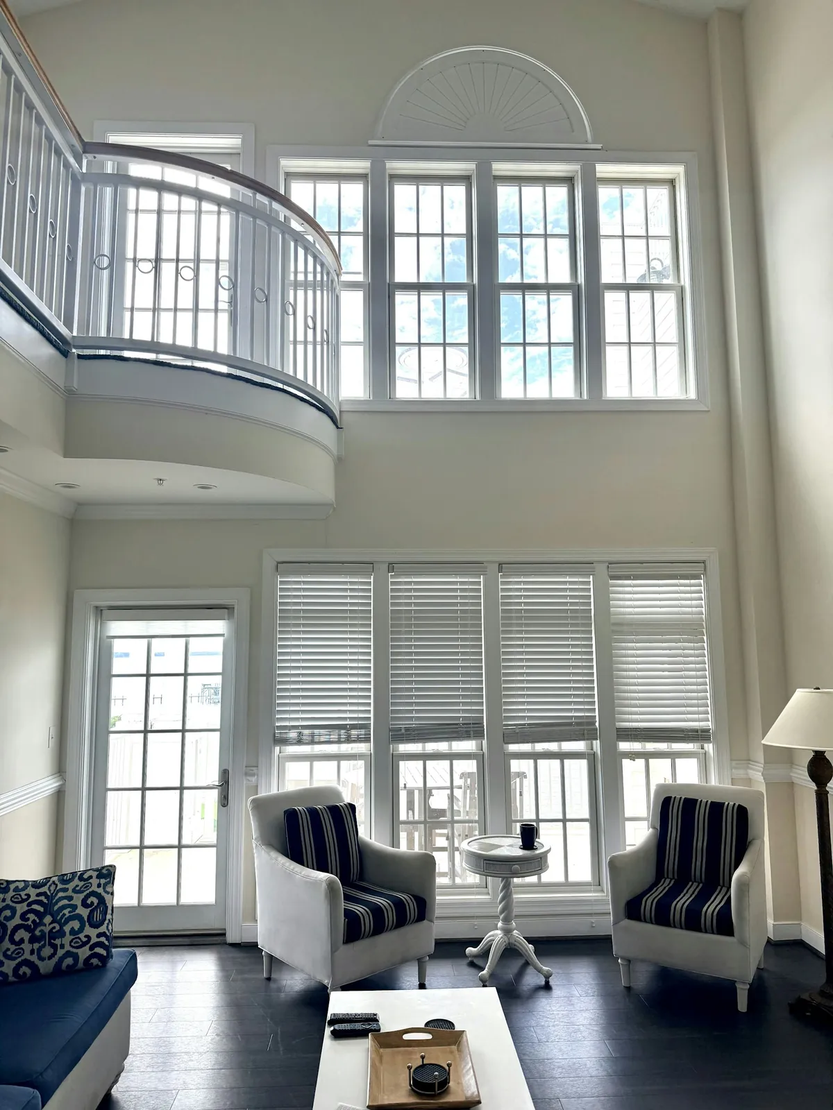 Two-storey living room with white shutters and blinds on tall windows below an arched window
