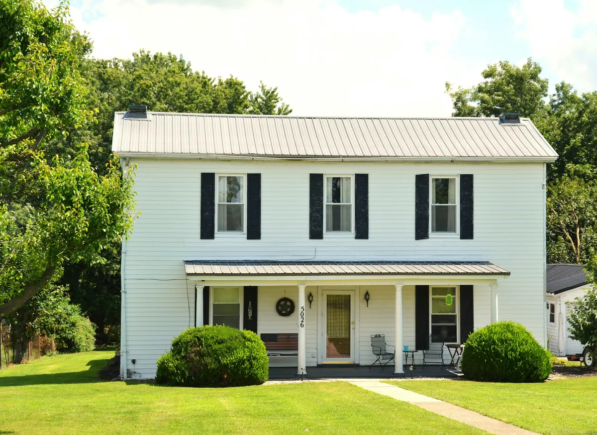 White two-storey farmhouse with black shutters and a front porch