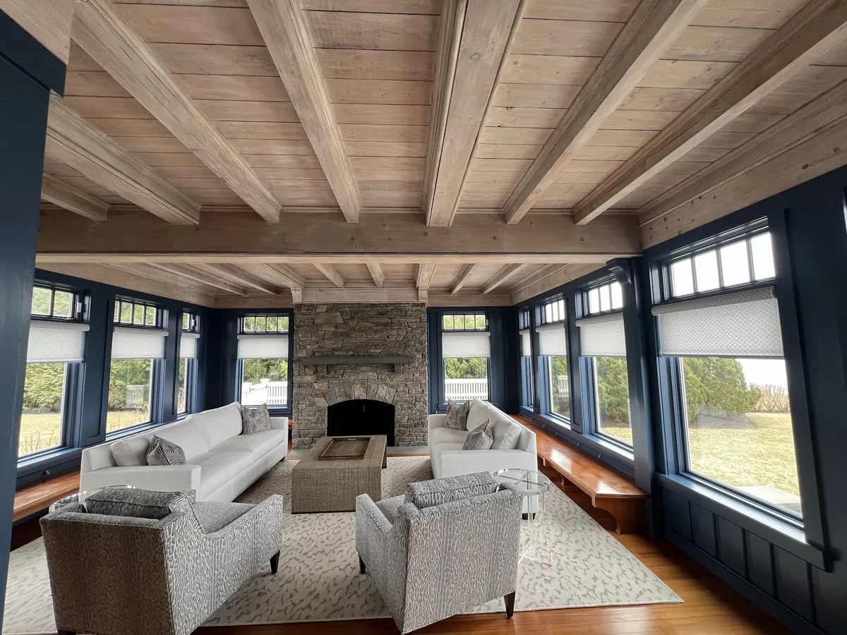 Sunroom with navy-framed windows, white roller shades on every window and a stone fireplace