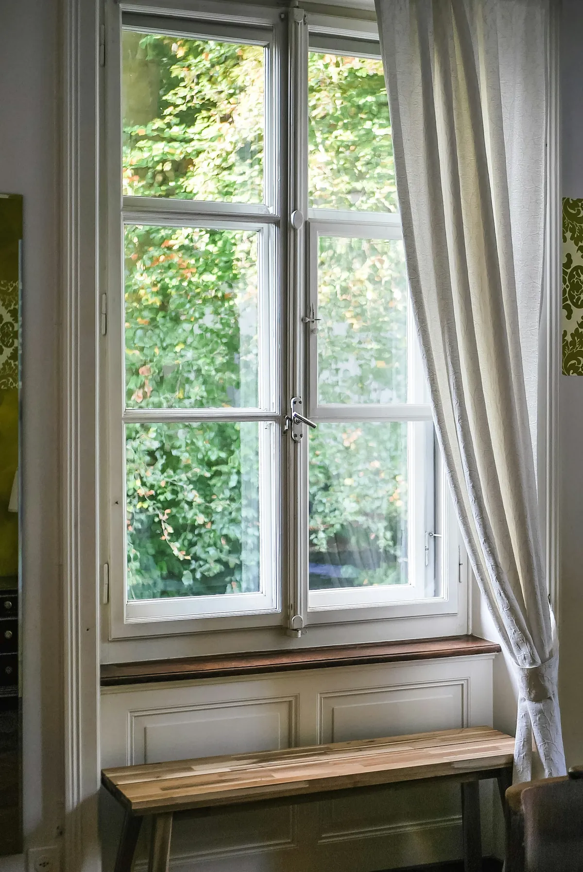 Tall casement window with a sheer side curtain above a window seat