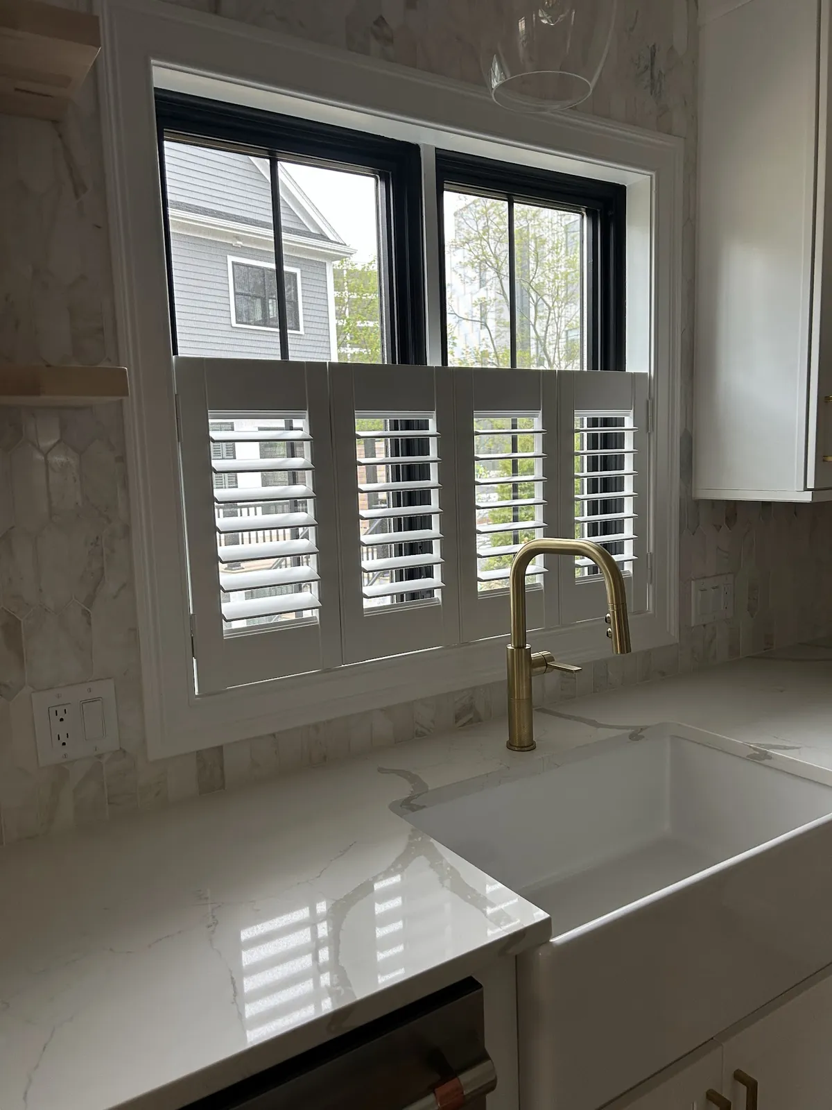 White cafe-style plantation shutters on a kitchen window above a farmhouse sink