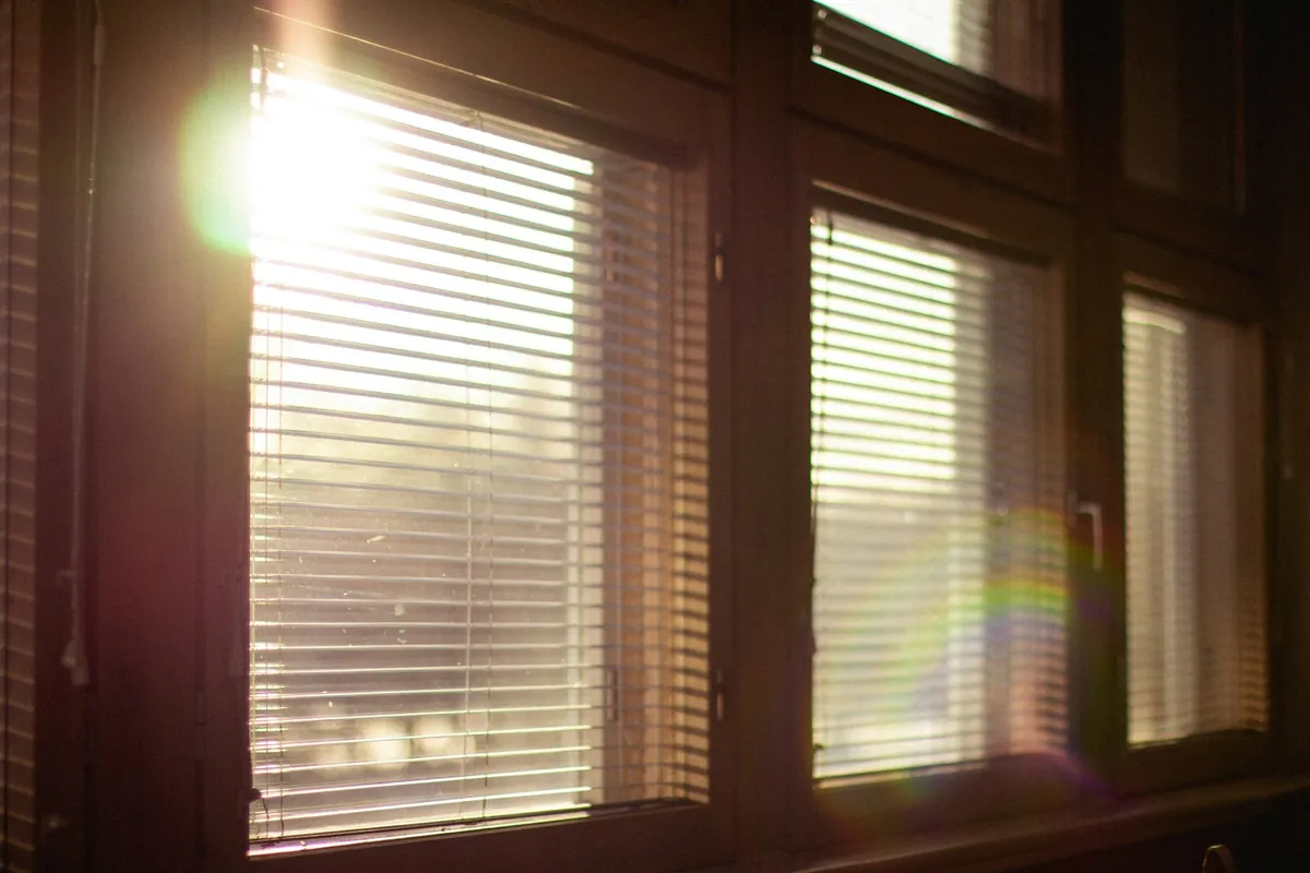 Horizontal blinds at a row of wood-framed windows with the sun behind them